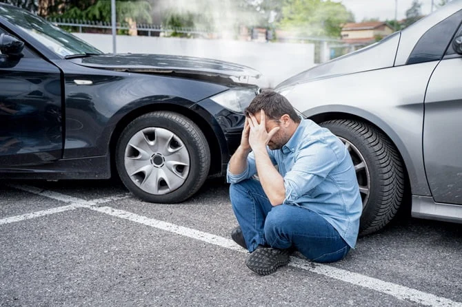 Driver sitting on the ground beside two crashed cars