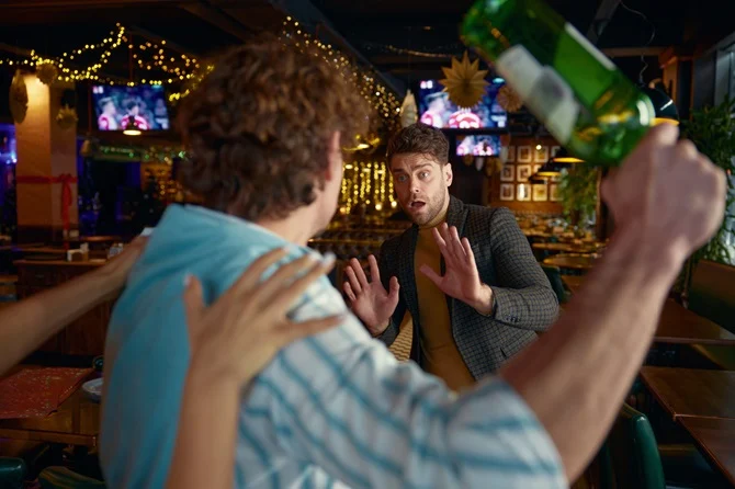 Drunk man swinging a bottle at another man in a bar