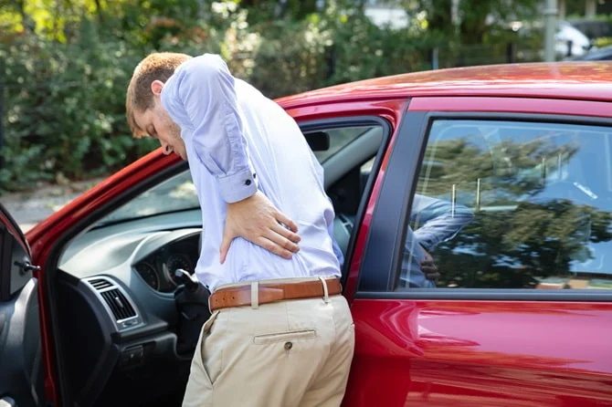 Man holding his back as he gets out of a car