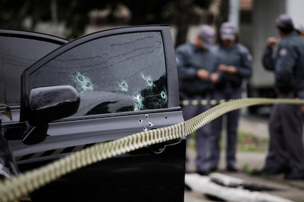 Police at a crime scene beside a bullet-riddled car